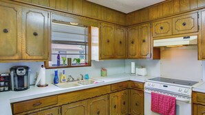 A kitchen with wooden cabinets, a stove, and a window with blinds. - Pet-friendly Cartwright Home w/ Private Backyard! (Cartwright)