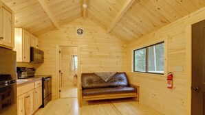 Ein Interieur einer Holzhütte mit einer Küchenzeile, einem Ledersofa und einem Fenster mit Blick ins Freie.