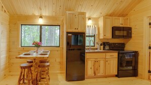 Eine Holzhüttenküche mit Kühlschrank, Herd, Mikrowelle und Holzstühlen um einen Tisch mit einer Blumenvase.