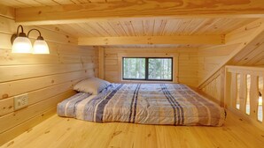 Ein Schlafzimmer in einer Holzhütte mit einem Bett, zwei Wandlampen, einem Fenster und einem Holgeländer.