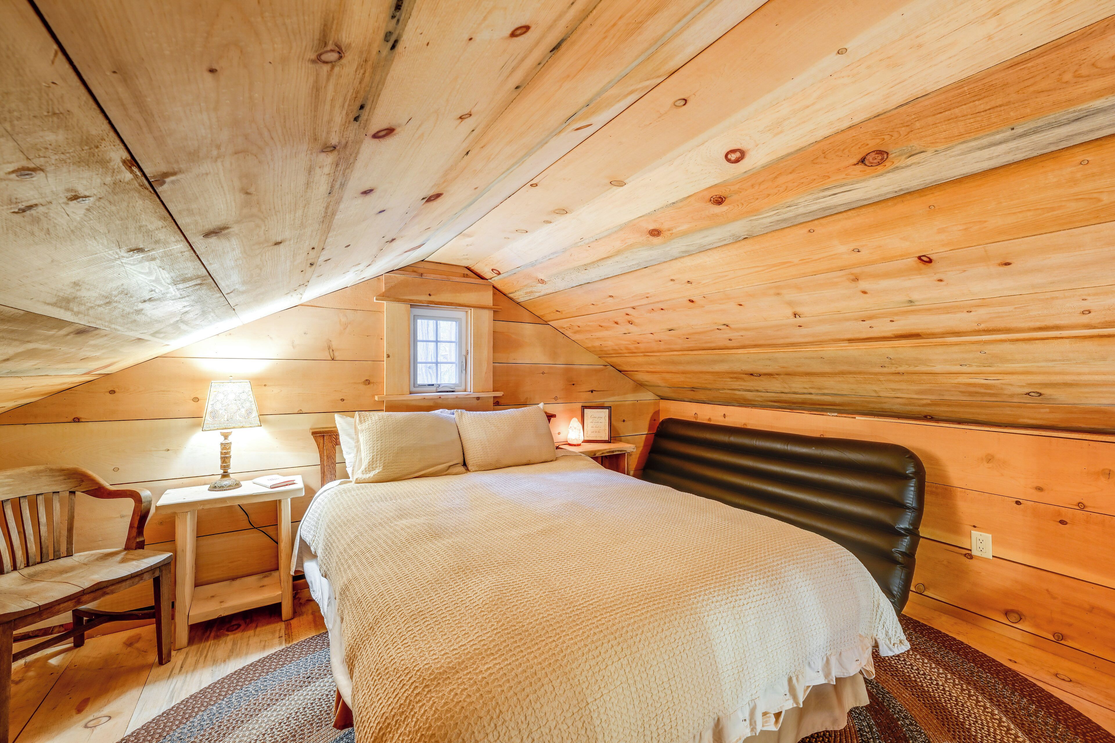 A cozy, wooden-paneled room with a bed, a chair, a small table, and a window.