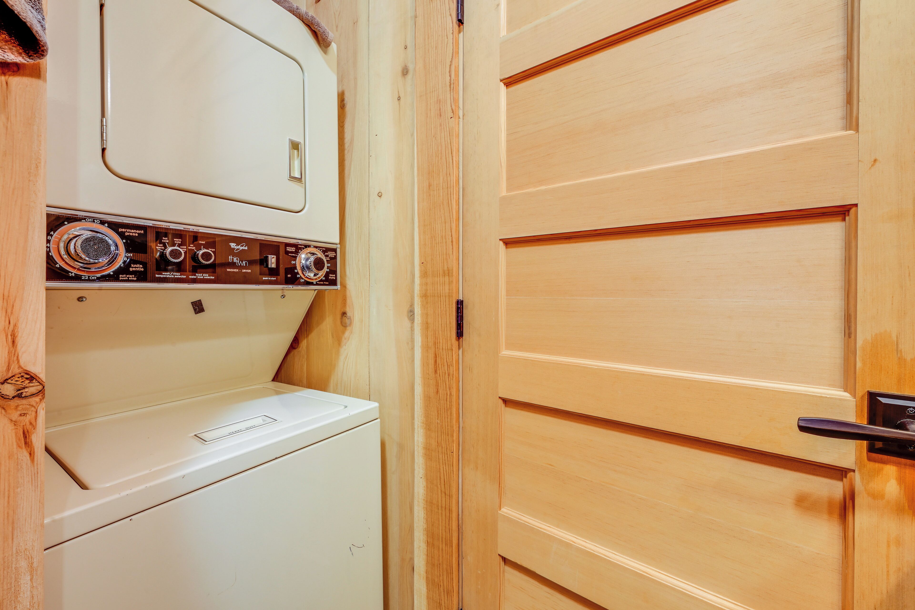 A laundry room with a white washer and dryer, wooden paneling, and a door with a handle.