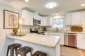A kitchen with white cabinets, a stainless steel dishwasher, a microwave, and a coffee maker. There are two stools at the island. - Charming Bamberg Home Near Medical Centers! (Bamberg)