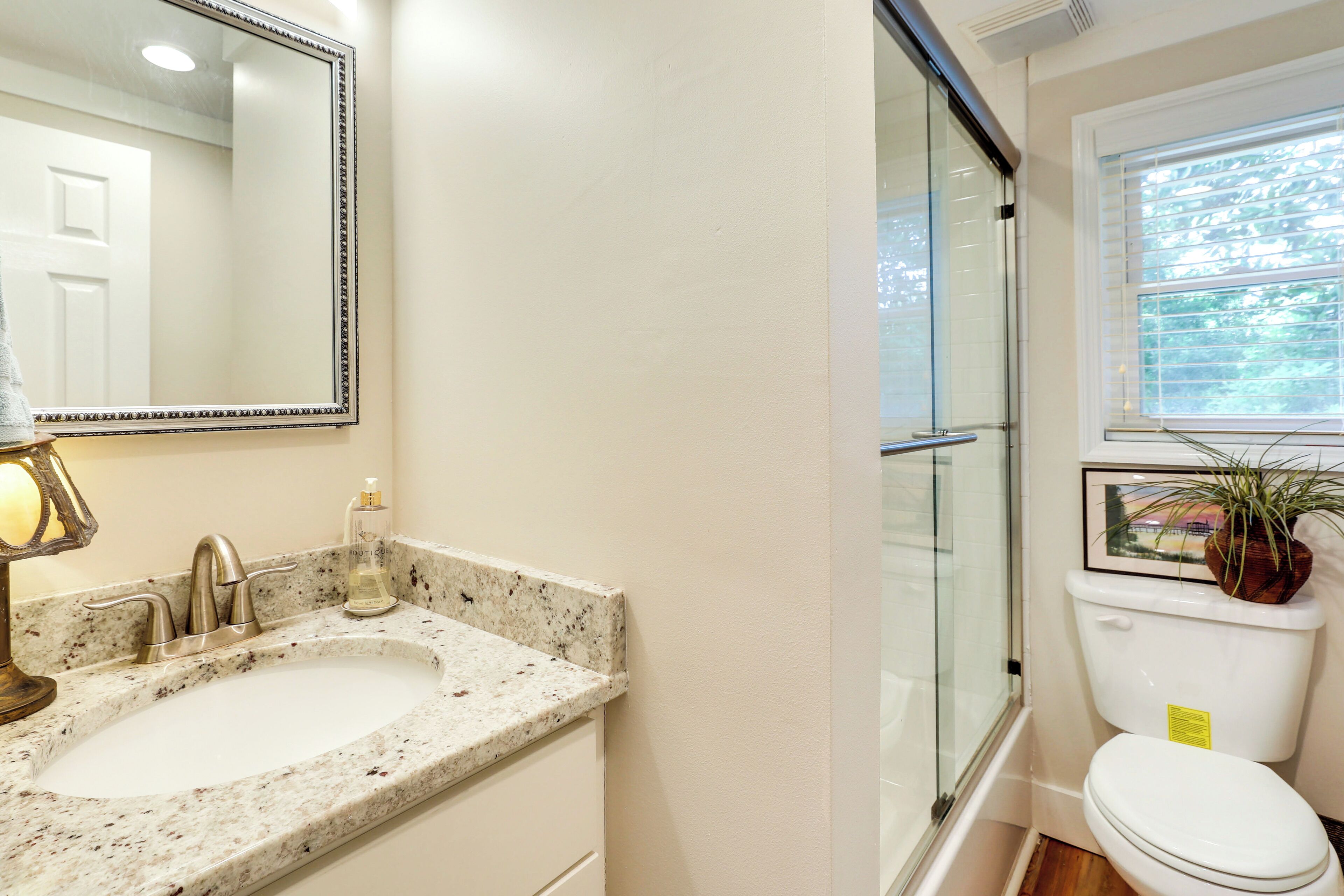 A bathroom with a sink, mirror, toilet, and window.