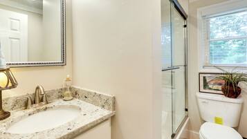 A bathroom with a sink, mirror, toilet, and window.