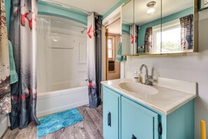 A bathroom with a bathtub, a sink, a mirror, and a blue mat on the floor. - Cozy Iowa Getaway w/ Patio & Fenced-in Yard! (Dyersville)