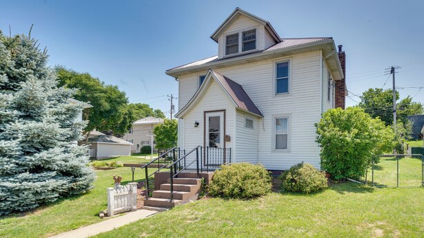 A two-story house with a front porch, a staircase, and a well-maintained lawn. - Cozy Iowa Getaway w/ Patio & Fenced-in Yard! (Dyersville)