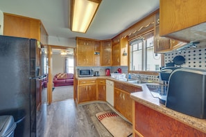 A compact kitchen with wooden cabinets, a refrigerator, microwave, and a sink. - Cozy Iowa Getaway w/ Patio & Fenced-in Yard! (Dyersville)