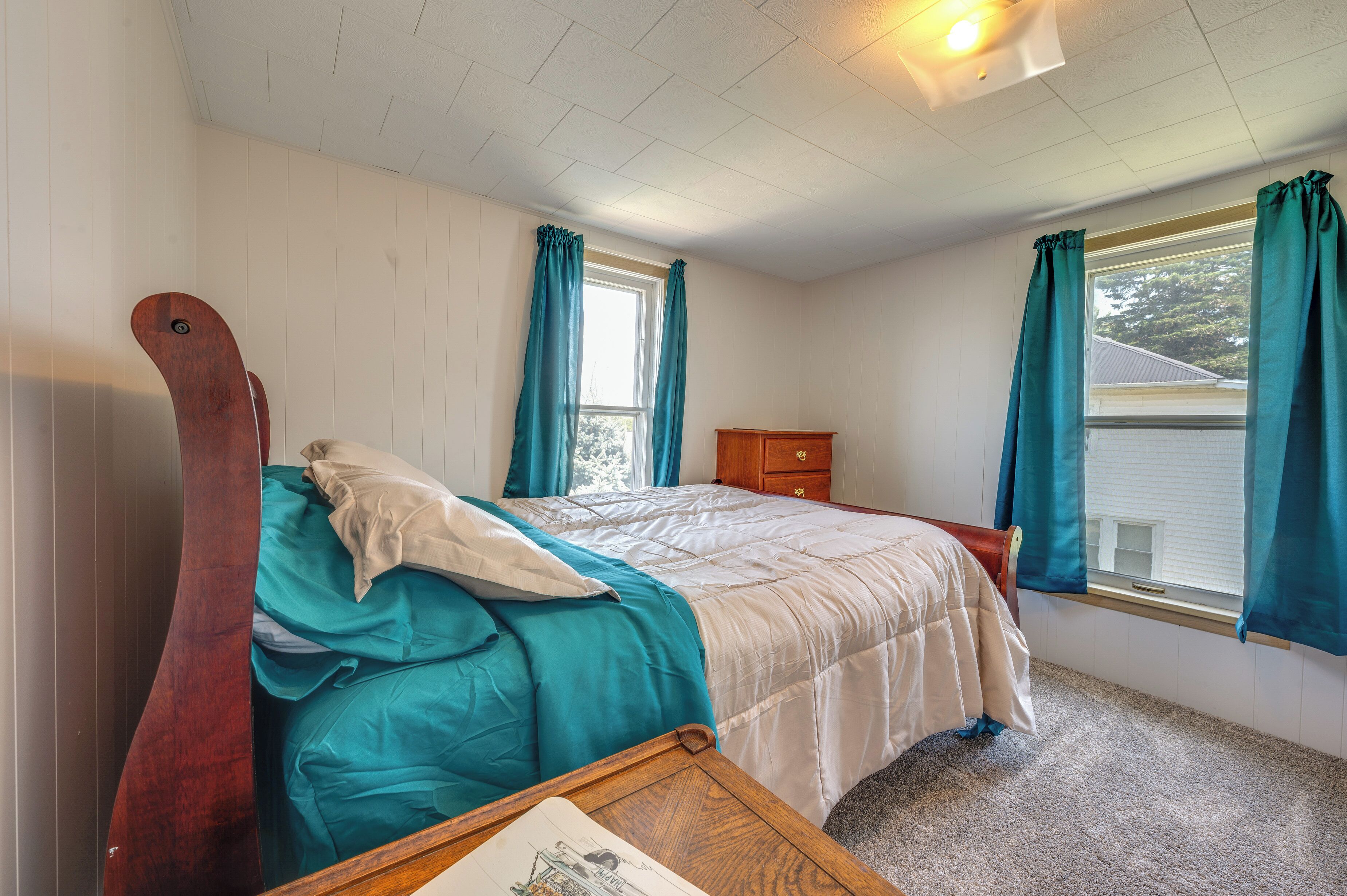 A bedroom with a single bed, a wooden headboard, a nightstand, a dresser, and a window with curtains.