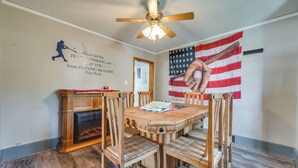 A dining area with a wooden table and chairs, a ceiling fan, and an American flag on the wall. - Cozy Iowa Getaway w/ Patio & Fenced-in Yard! (Dyersville)