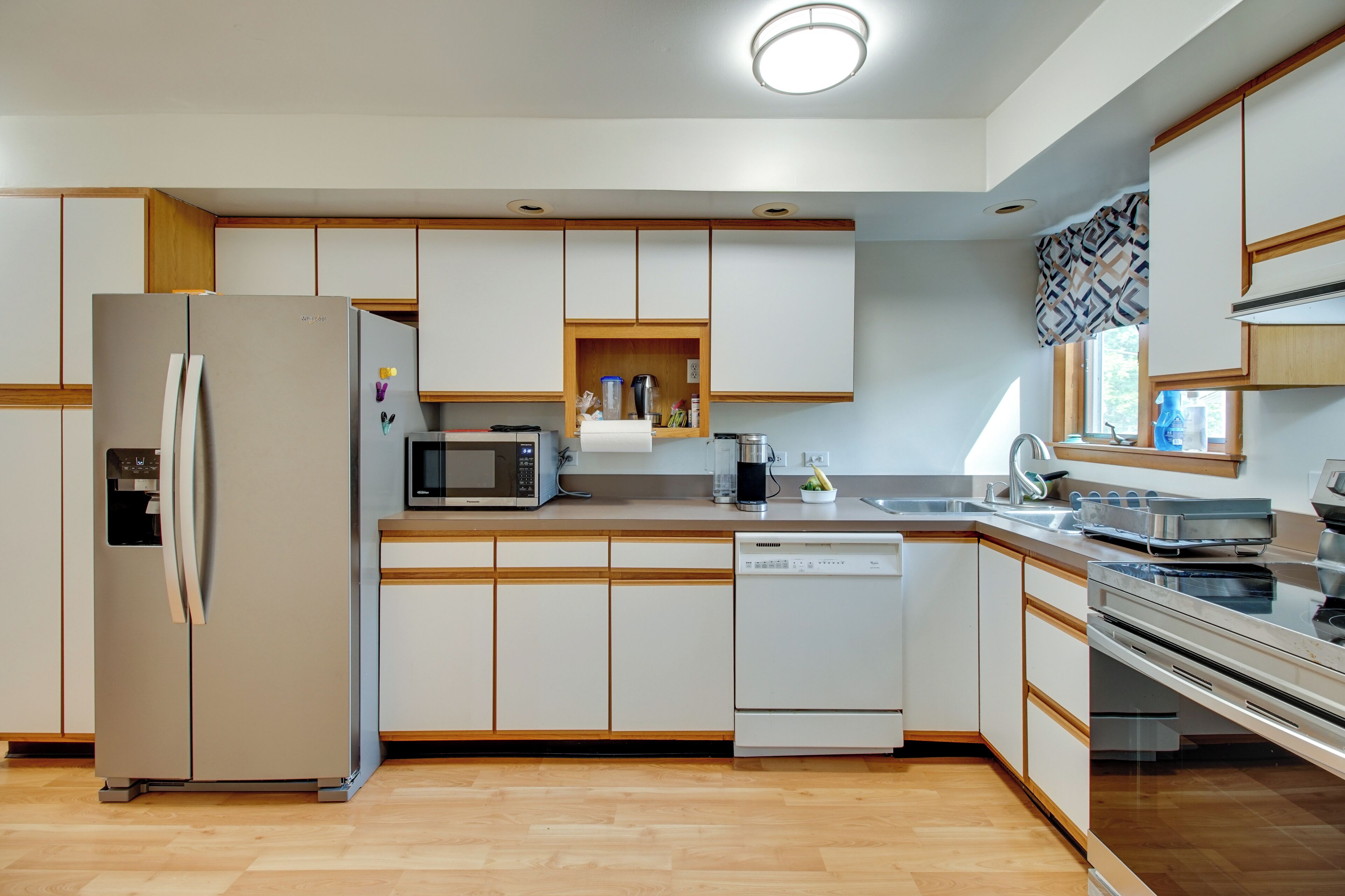 Una cocina moderna con refrigerador, microondas, lavavajillas y una ventana con cortinas estampadas.