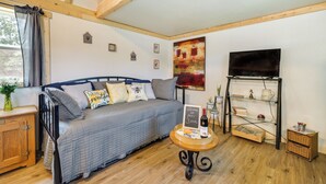 A cozy room with a bed, a small table with a tray, a bookshelf, and a TV on the wall. - Charming Oklahoma Retreat w/ Grill - Pets Welcome! (Spencerville)