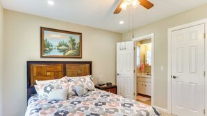 A bedroom with a bed, a wooden headboard, a ceiling fan, and a painting on the wall.