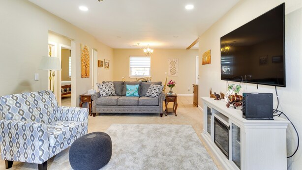 A living room with a sofa, armchair, ottoman, fireplace, television, and ceiling fan.
