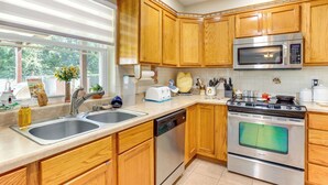 A modern kitchen with wooden cabinets, stainless steel appliances, a double sink, and a window with a view of greenery.