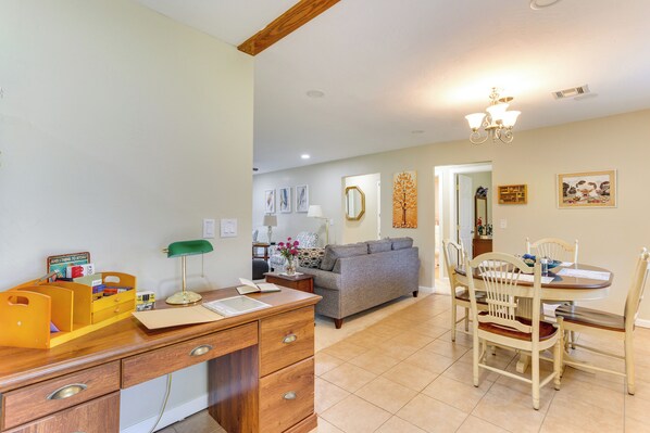 A well-lit room with a wooden desk, a sofa, and a dining table with chairs.