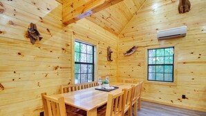 A wooden cabin interior with a dining table, chairs, two windows, and a mounted air conditioner. - Crystal Springs Cabin, 4 Mi to Calling Panther! (Crystal Springs)