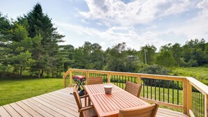 Une terrasse en bois avec une table et des chaises, entourée d’une balustrade en bois, donnant sur une zone herbeuse parsemée d’arbres.