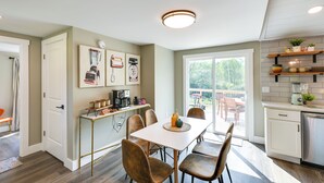 Une cuisine moderne avec un coin repas, comprenant une table blanche, des chaises marron et une vue sur l’extérieur.