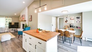 Une cuisine moderne dotée d’un îlot central en bois, de meubles blancs et d’un coin repas avec des chaises en bois.