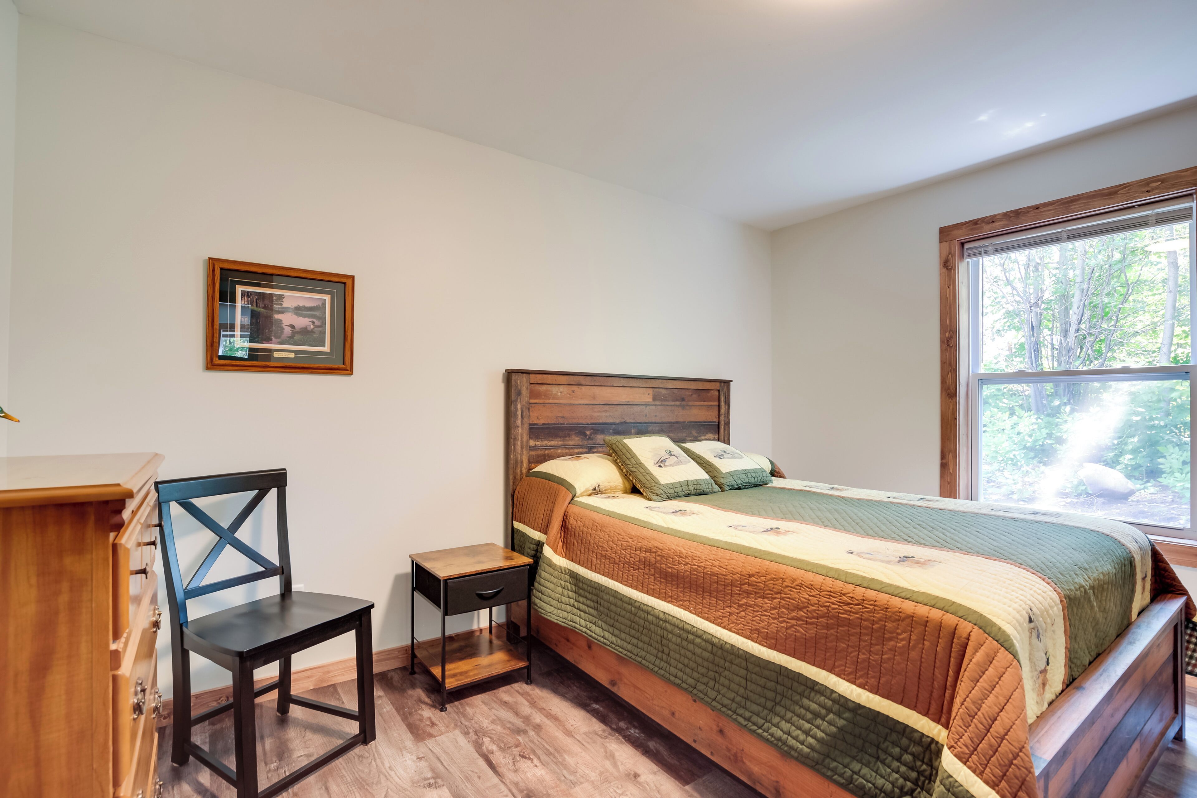 A bedroom with a wooden bed, a nightstand, a chair, and a dresser.