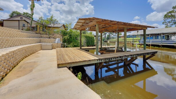 A wooden deck over a body of water with a pergola structure, surrounded by a brick wall and greenery.