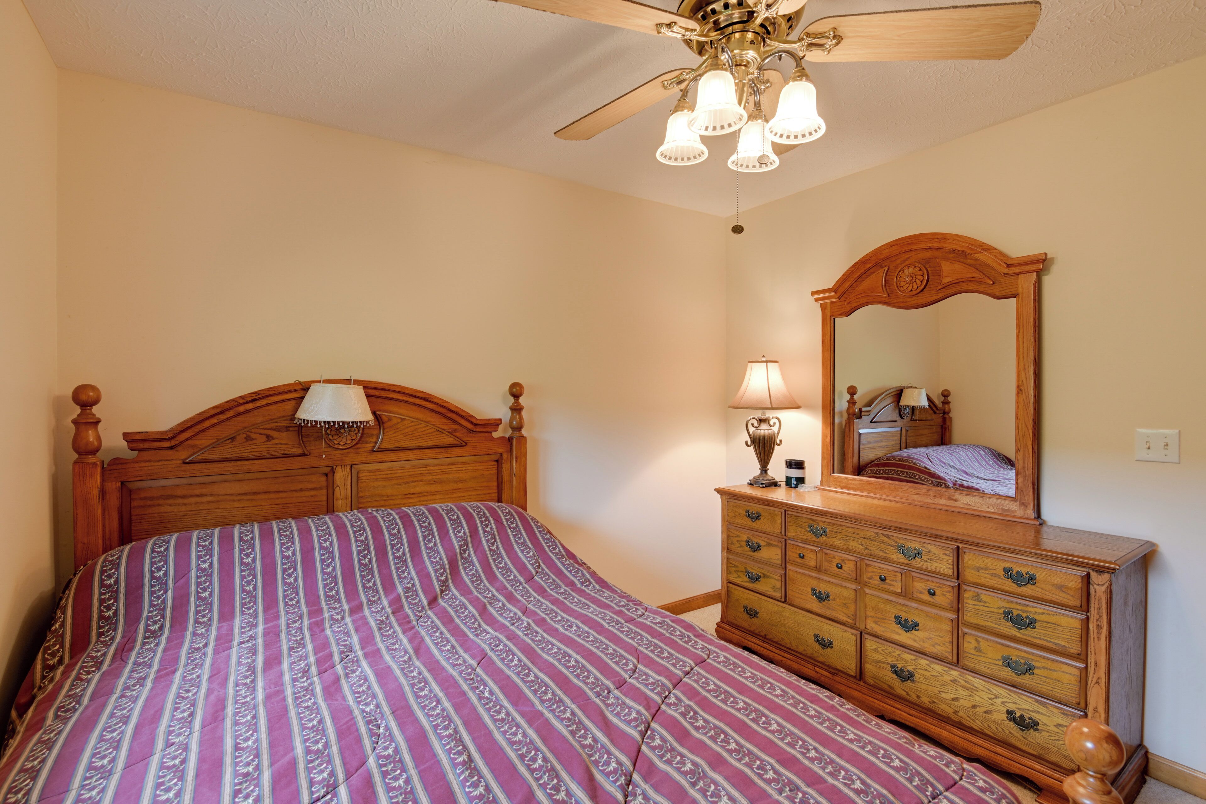 A bedroom with a wooden bed, a dresser, a mirror, and a ceiling fan.