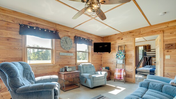 Ein gemütliches Cabin-Interieur mit Holzwänden, einem Deckenventilator, einem großen Fenster und einem an der Wand befestigten Fernseher.