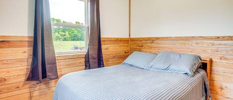 Un dormitorio con cabecera de madera, una cama con colcha estampada y una ventana con cortinas.