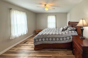 A bedroom with a bed, a ceiling fan, a nightstand, and a lamp.