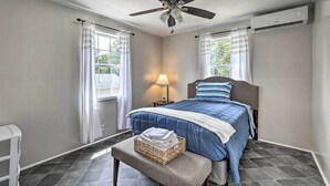 A bedroom with a bed, a ceiling fan, an air conditioning unit, a bedside lamp, and a window with curtains. - Spacious Family Home on Lake Marion w/ Boat Ramp! (Cameron)