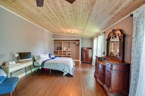 Une chambre avec un plafond en bois, un lit recouvert d’une couvre-lit à motifs, une commode avec un miroir et un bureau avec un ordinateur et une lampe.