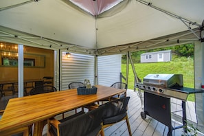 Un espace extérieur aménagé en patio, avec une table en bois, des chaises, un barbecue et un espace abrité.