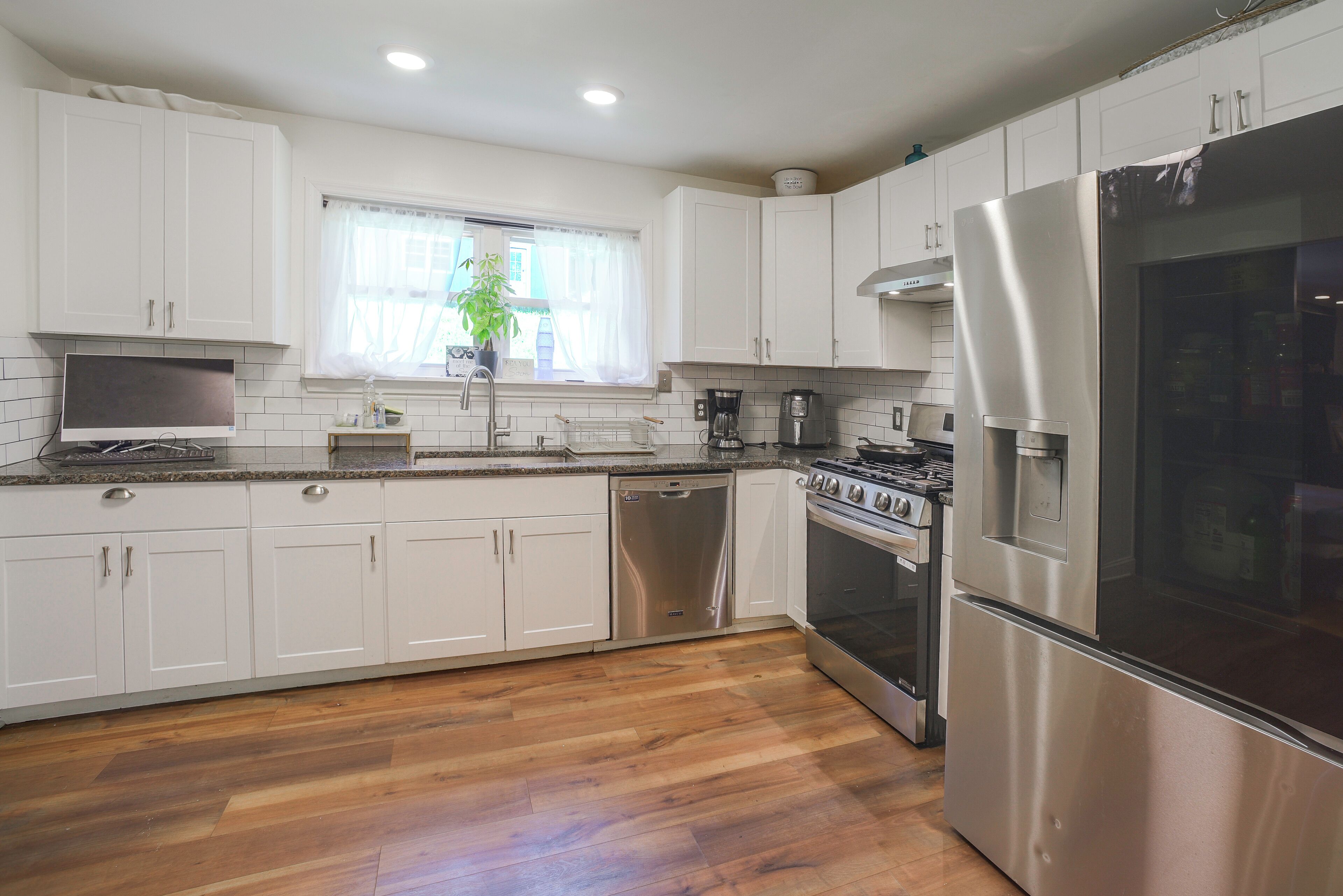A modern kitchen with white cabinets, stainless steel appliances, and a wooden floor.