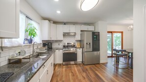 Une cuisine moderne avec des meubles blancs, des appareils en acier inoxydable, un plan de travail en granit et un plancher en bois.