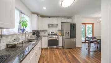 A modern kitchen with white cabinets, stainless steel appliances, a granite countertop, and a wooden floor.