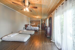 Un dormitorio con techo de madera, ventilador de techo, cama con ropa de cama floral, cómoda y ventana con cortinas de gasa.