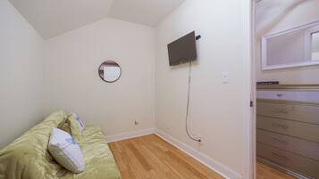 A bedroom with a bed, a round mirror, a flat-screen TV mounted on the wall, and a dresser with drawers.