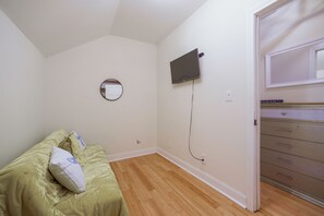 Une chambre à coucher comprenant un lit, un miroir rond, un téléviseur à écran plat fixé au mur et une commode avec des tiroirs.