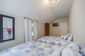 Une chambre avec deux lits, un téléviseur fixé au mur et un tableau encadré représentant la Tour Eiffel.