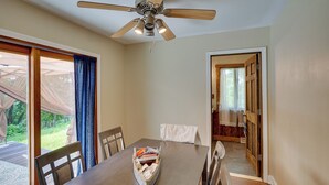 Un coin repas avec une table en bois, des chaises et un ventilateur de plafond. On peut apercevoir une terrasse à travers une porte vitrée.