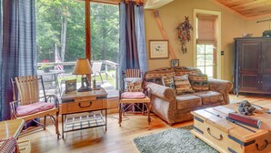 A cozy living room with a wooden floor, a leather sofa, a wooden coffee table, and a large window with curtains.