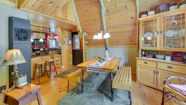 A cozy cabin interior with a wooden dining table, benches, a kitchen area, and a cabinet with glass doors.