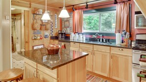 A kitchen with wooden cabinets, a granite countertop, a coffee station, and a window with curtains.