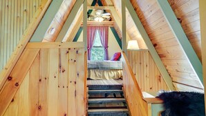 A wooden staircase leading to a bedroom with a bed, a window with curtains, and a ceiling fan.