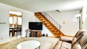 Un salon avec un canapé en cuir marron, une table ronde blanche, un escalier en bois et un téléviseur à écran plat.