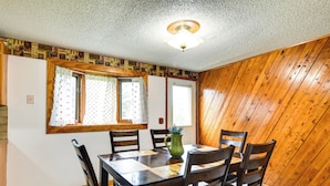 Un coin repas avec une table et des chaises en bois, un pichet vert et une fenêtre avec des rideaux.