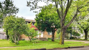 Une maison à deux étages, construite en briques, avec un jardin devant, une allée et un trottoir.