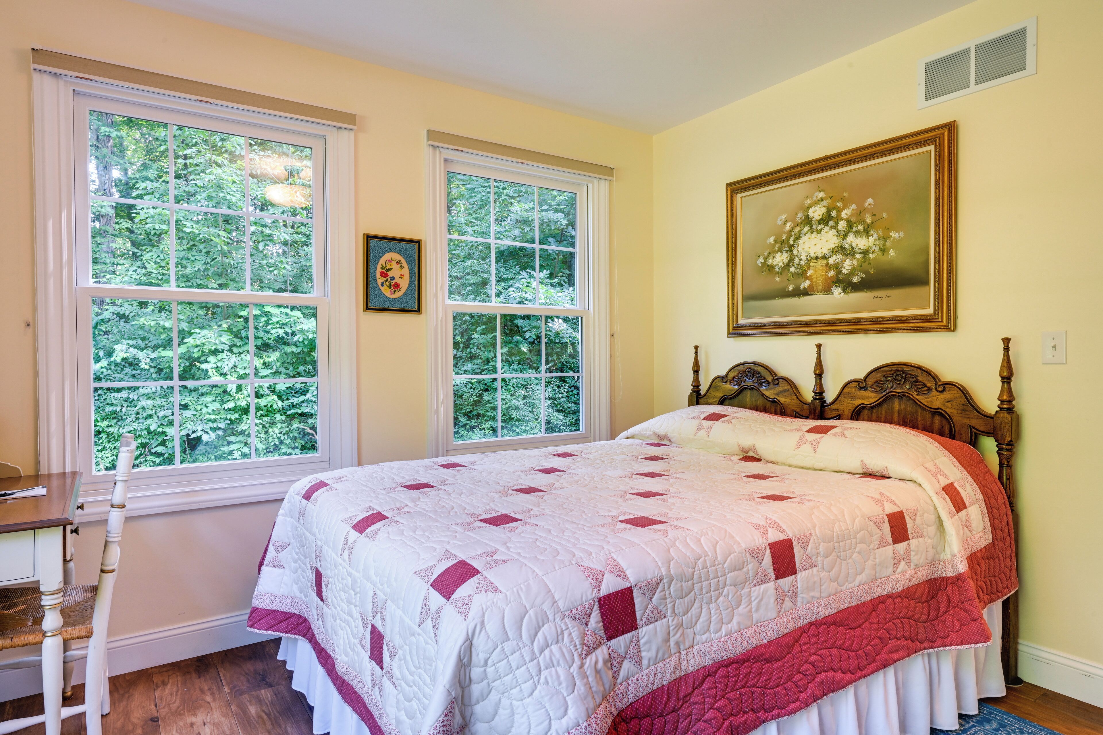 A bedroom with a large bed, two windows, a wooden headboard, and a framed picture on the wall.