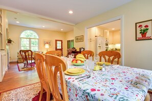 Un coin repas avec une nappe à motifs floraux, des chaises en bois et un panier de fruits posé sur la table.